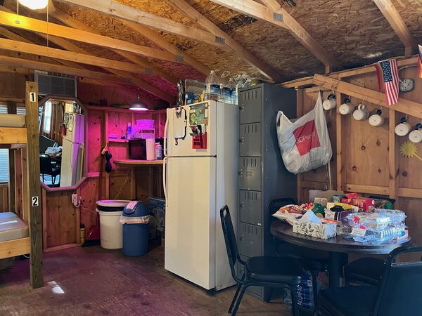 Bunkhouse kitchen area with a full-size refrigerator, a counter with a microwave, gray lockers and a round table with chairs
