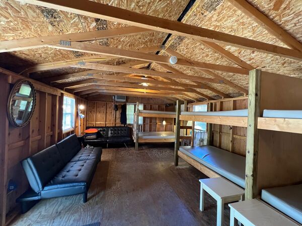 Bunkhouse interior with two black fold-down couches along one wall and numbered wooden bunk beds along the other, under exposed rafters