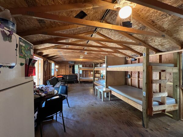 Length of the bunkhouse from the refrigerator end, past a table with chairs and the couches to numbered bunk beds along the right wall