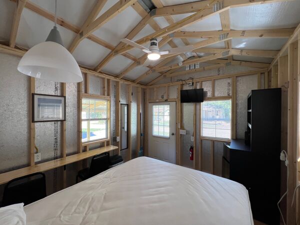 Long wooden counter with two chairs along the windows, the front door and mounted television ahead and a black storage unit to the right