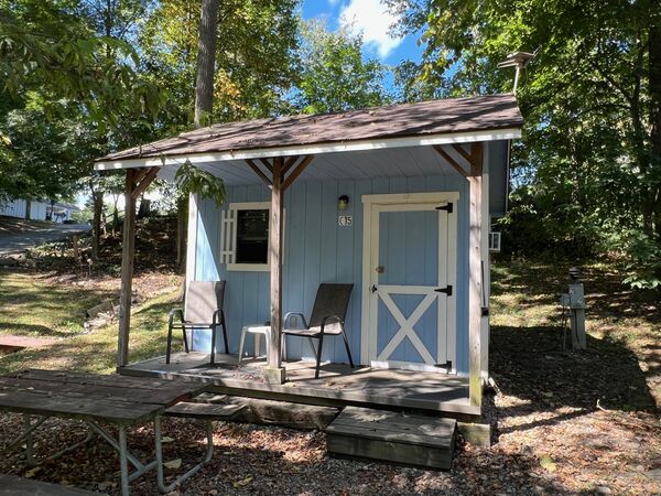 Covered porch of a light blue cabin with two chairs and a small white table beside a white barn-style door, a picnic table in front