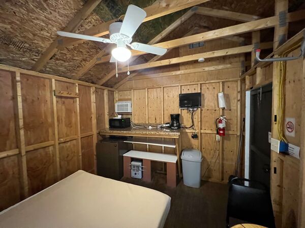 Kitchenette counter with a microwave, coffee maker and mounted television above a mini fridge and trash can, with a wall air conditioner