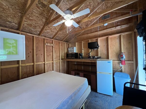 Corner kitchenette with a microwave, coffee maker and small television on the counter, a white refrigerator and a wall air conditioner