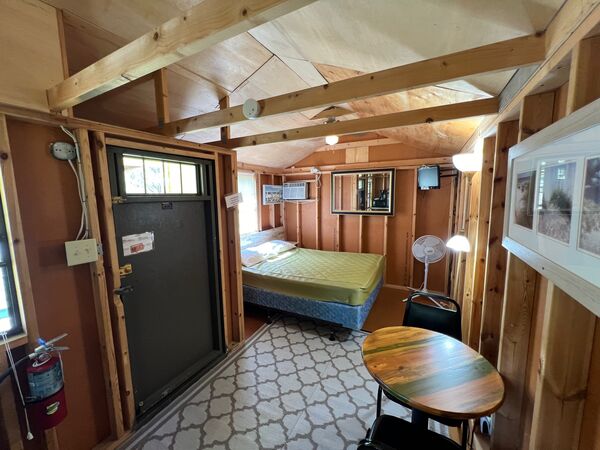 Interior looking from the door toward the queen bed, with a wall air conditioner, mounted television, mirror and a round table with chairs