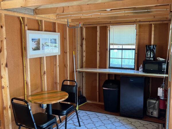 Kitchenette counter under a window with a coffee maker and microwave above a mini fridge, beside a round table and two chairs