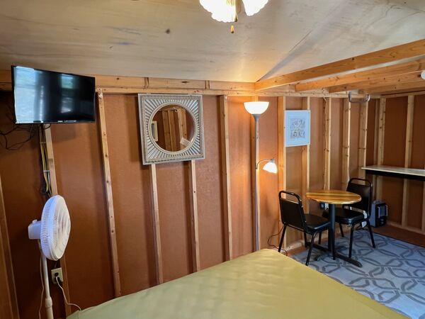 Corner of the cabin with a wall-mounted television, a framed mirror, a floor lamp and a round table with two chairs by the kitchenette counter