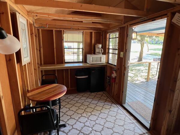 Kitchenette counter under a window with a coffee maker and microwave, a mini fridge and trash can below, and the open door to the deck