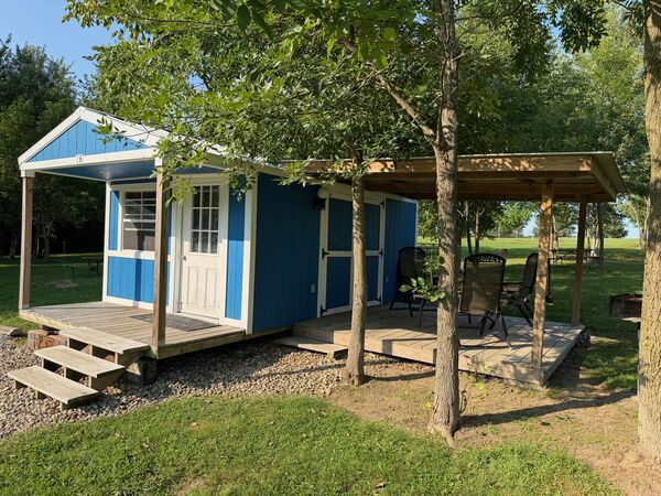 Blue cabin from an angle, showing the small front porch with steps and the larger covered side porch with folding chairs