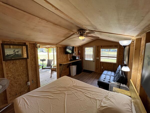 View from the foot of the bed across the couch and kitchenette to the front door and the open double doors onto the covered porch