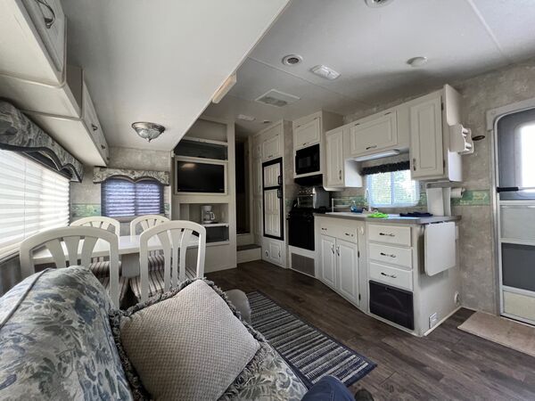 Kitchen with white cabinets, a propane stove with a microwave above, a refrigerator and a sink under a window, past the dining table