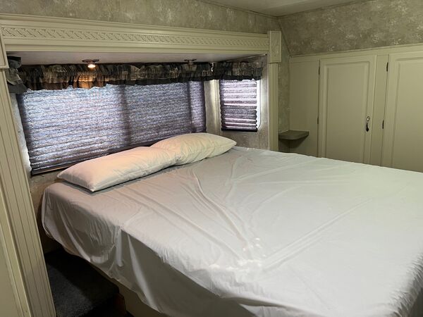 Bedroom with a queen bed and two pillows beneath a wide window, and a built-in white closet