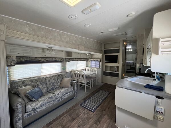 Floral sofa and dining table by the windows, a television in the cabinetry, and the kitchen counter and sink
