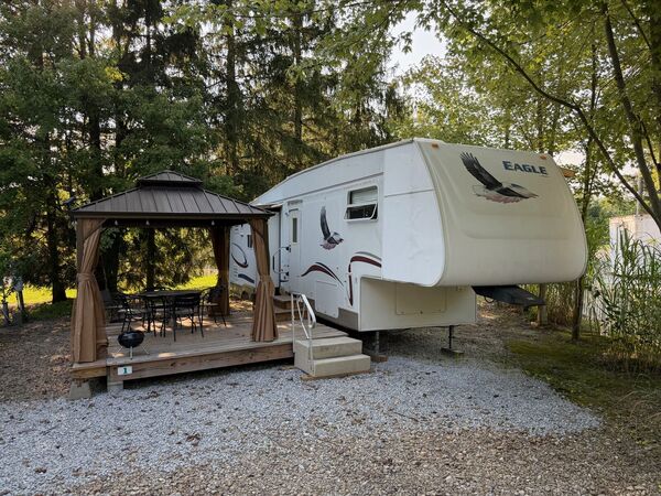 Eagle fifth-wheel trailer with an eagle decal, beside a wooden deck with a curtained gazebo over a dining table and chairs