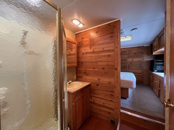 Bathroom with a glass shower and a vanity sink against cedar paneling, the bedroom and queen bed beyond