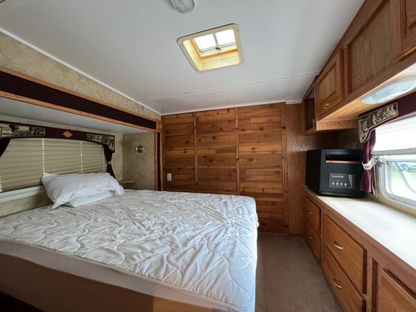 Bedroom with a queen bed under a skylight, cedar-paneled walls, a dresser counter beneath a window and a space heater