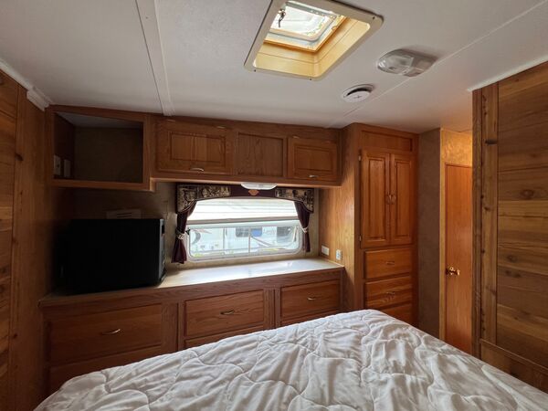 Foot of the queen bed facing a window with drawers and cabinets, a small television, and a closet under a skylight