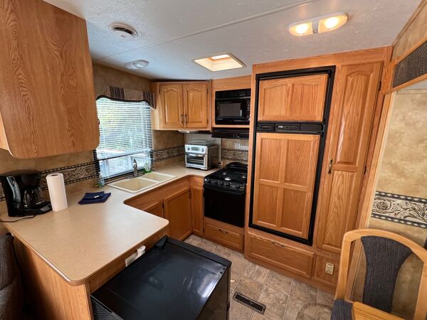 Kitchen with a sink under a window, a propane stove with a microwave above, an air fryer oven, coffee maker and a full-height refrigerator