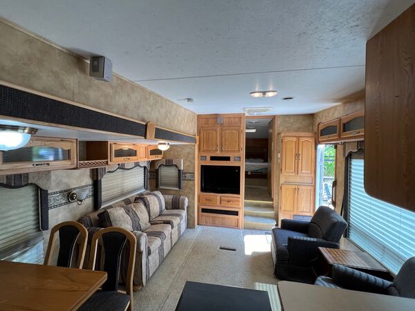 Living room toward the front of the trailer: a striped sofa, two armchairs, a television in the cabinetry and steps up to the bedroom