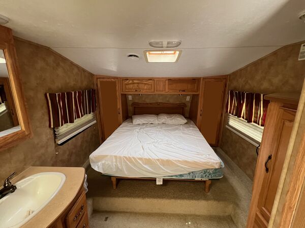 Bedroom with a queen bed between two curtained windows, closets on each side and a vanity sink in the foreground