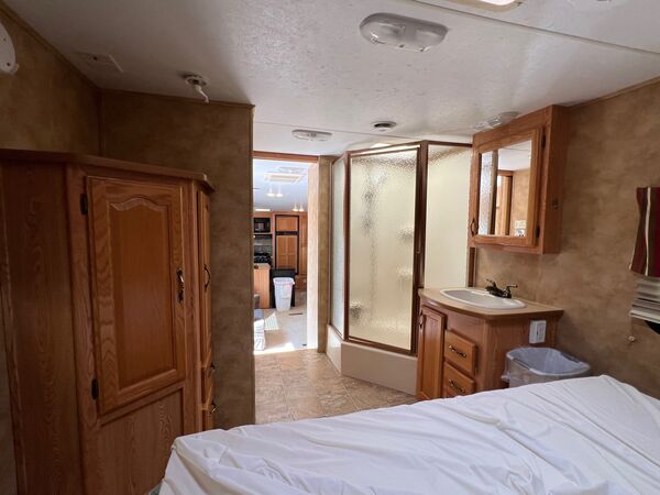 From the bed: a wardrobe, a glass shower and a vanity sink with a mirrored cabinet, with the kitchen visible down the hall