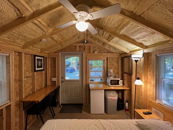 From the bed toward the front door: a long counter with two chairs, a kitchenette with a microwave, coffee maker and mini fridge, and a floor lamp
