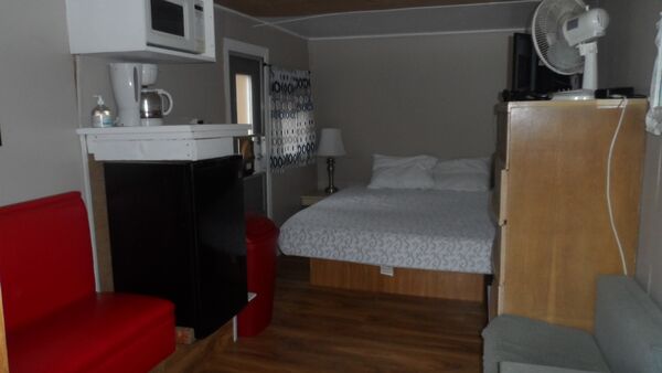 Inside the Roamer: a red bench seat, a coffee maker and microwave over a mini fridge, a bed at the far end and a dresser with a fan and television
