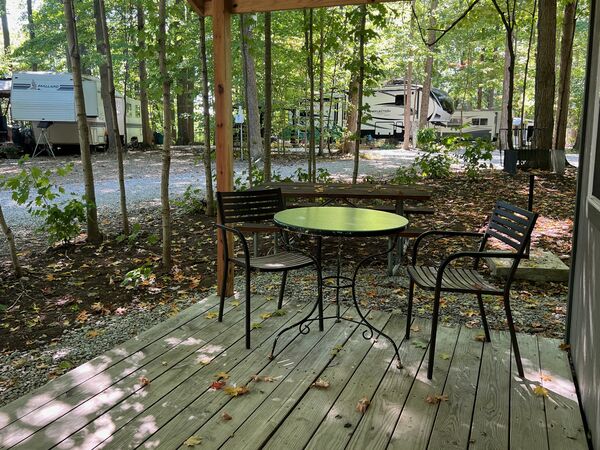 Covered deck with a green bistro table and two black chairs, looking out over a picnic table to wooded RV sites