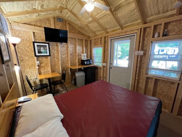 From the bed toward the front door: a mounted television, a small table with two chairs, and a counter with a microwave beside the door